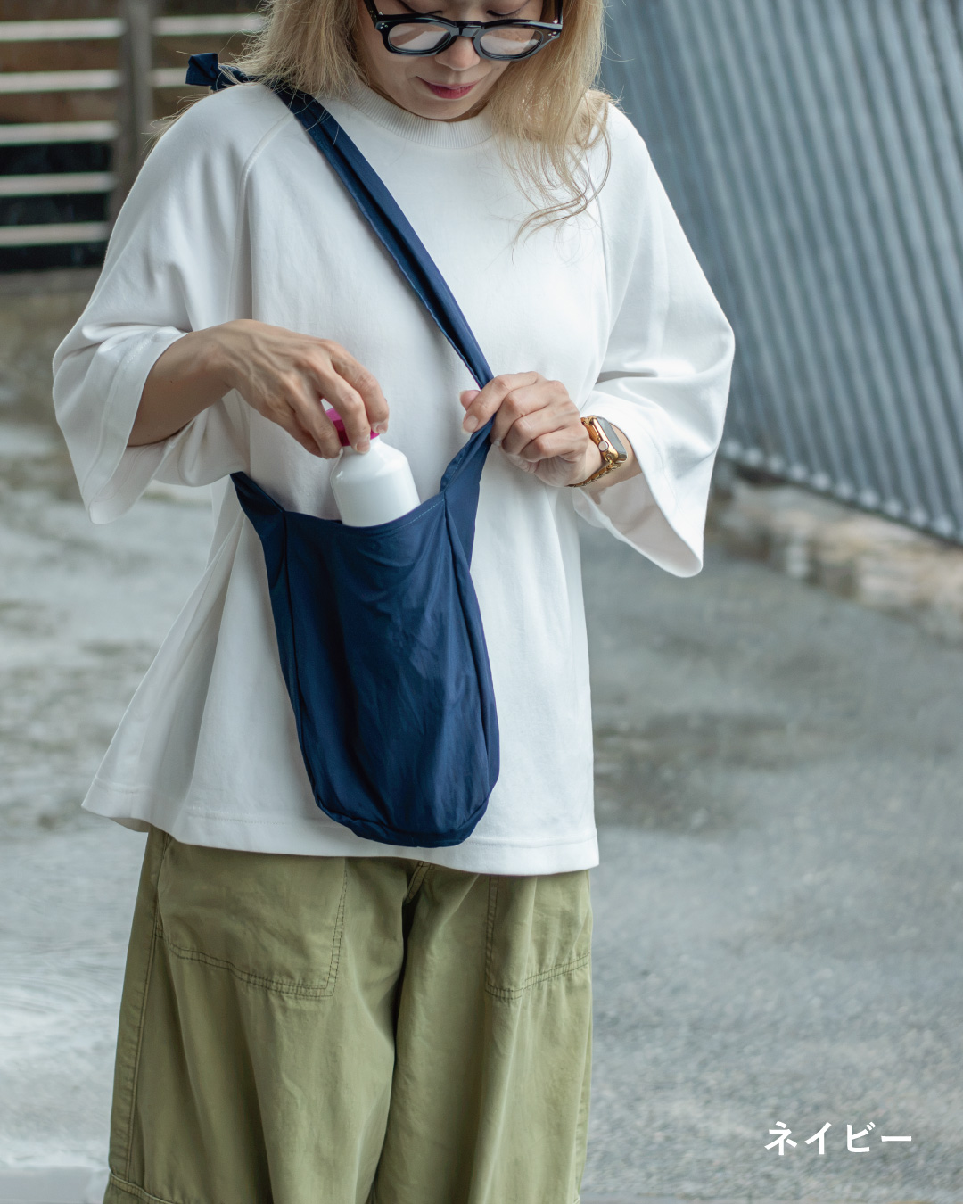 NOMAD SLING(Tav-051)のネイビーにボトルを入れる様子を写した、開口部の使いやすさが分かるカット。
