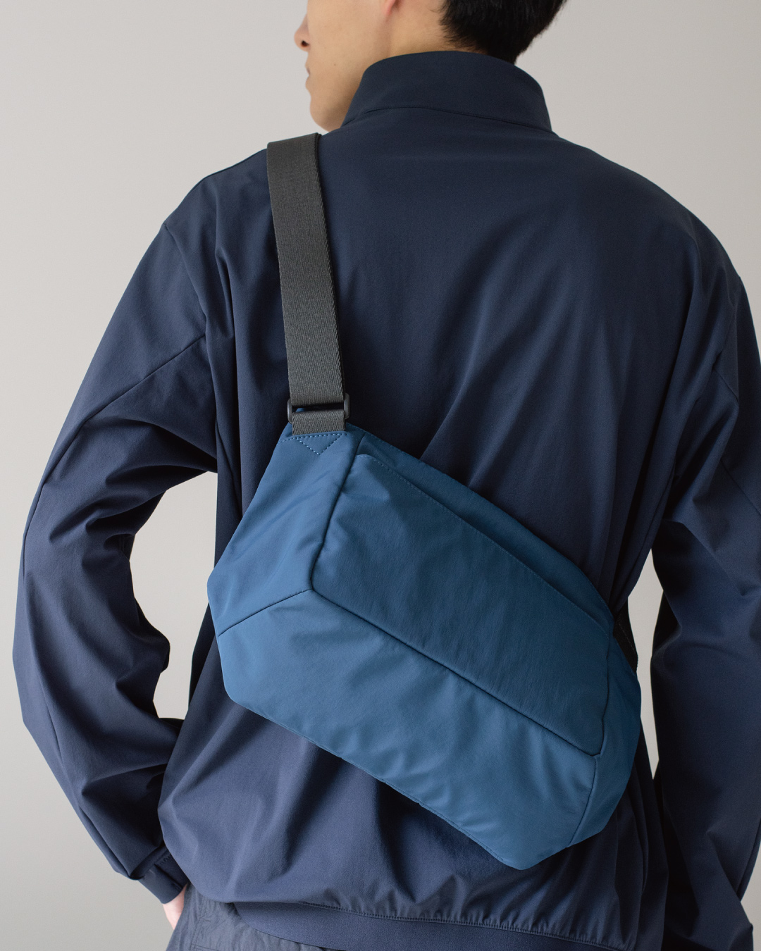 男性がネイビーのメンズショルダーバッグを背中に背負っている姿。バッグの背面からの見た目。 