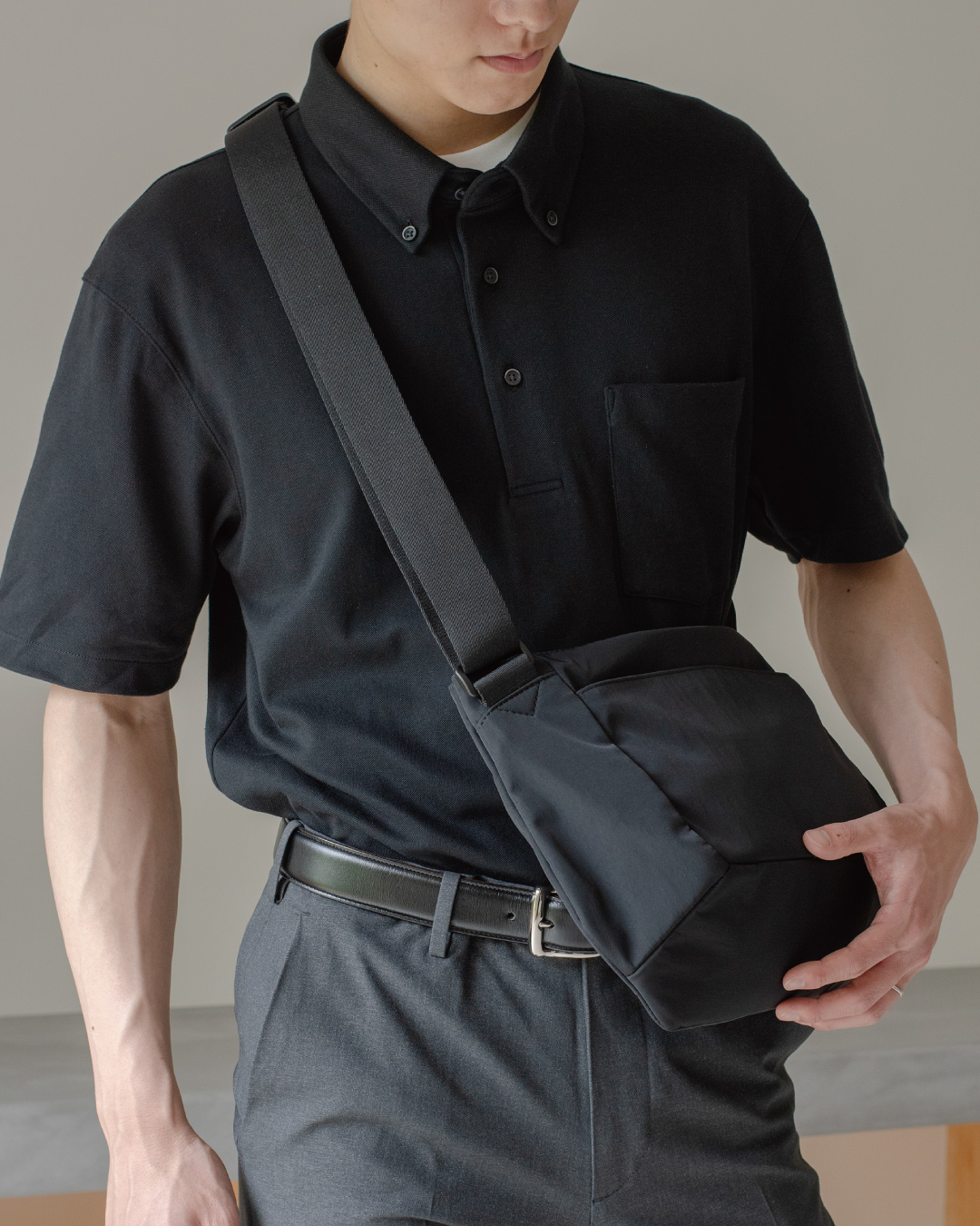 男性がブラックのメンズショルダーバッグを斜めがけにしている全身ショット。シンプルなデザインが特徴。  