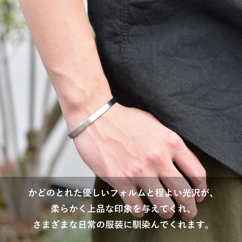 かどのとれた優しいフォルムと程よい光沢で、黒いリネンシャツなど日常の服装に上品に馴染むTVRT 真鍮バングルの着用イメージ