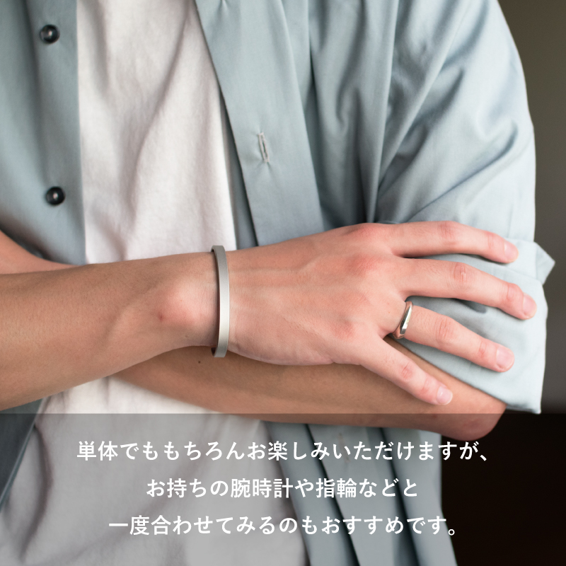 淡いブルーのシャツに合わせ、指輪との重ね付けも楽しめるTVRT 真鍮バングルを腕組みした手首に着けたメンズコーデ