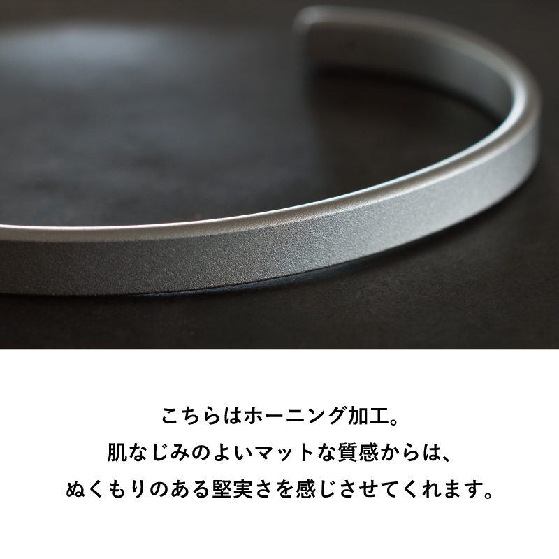 肌なじみのよいマットな質感でぬくもりある堅実さを感じさせる、ホーニング加工仕上げのTVRT 真鍮バングルを黒背景でアップ