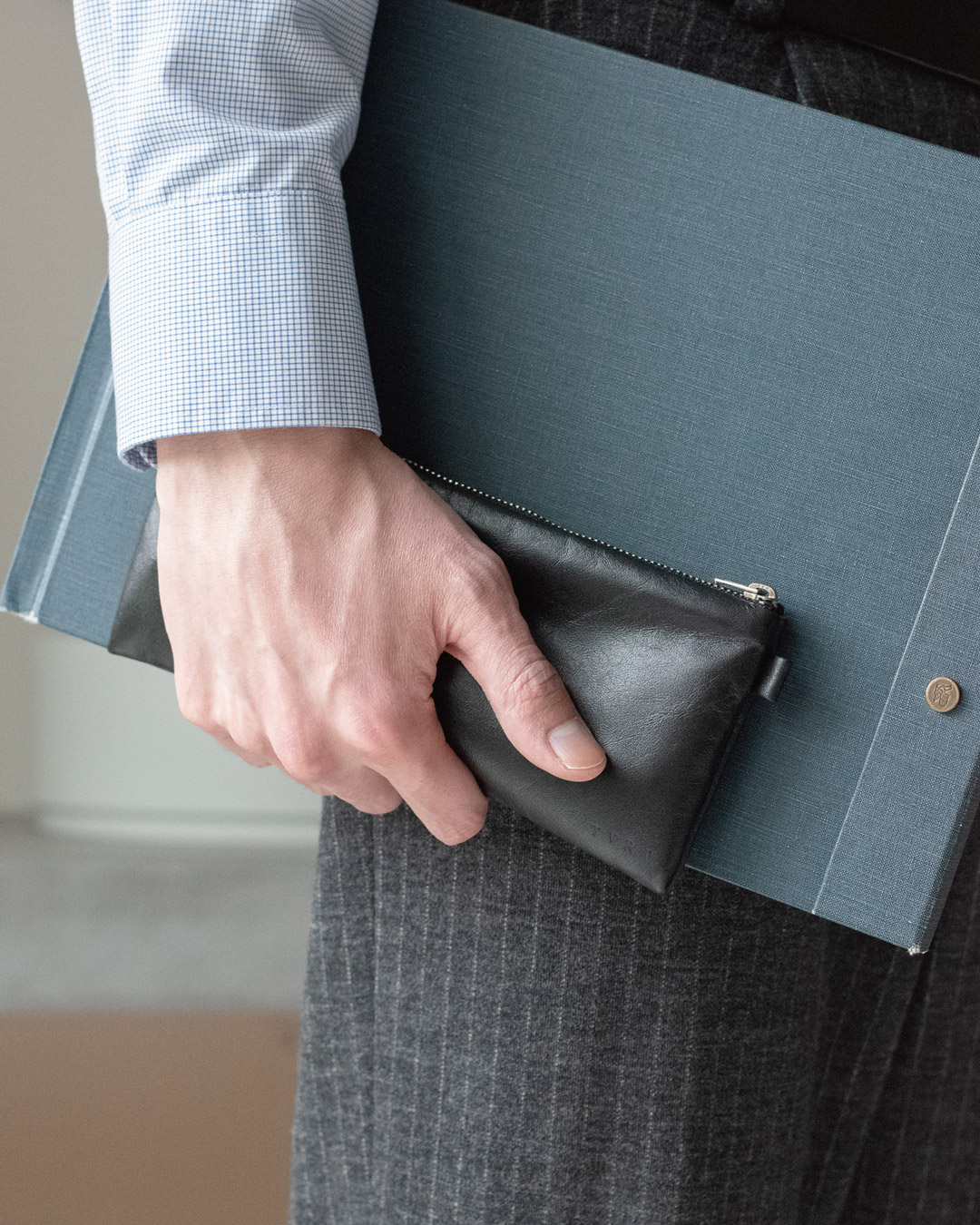 スーツ姿でFOLMAレザーポーチPENとクリップボードを一緒に手持ちするビジネスシーン。細長いPENサイズがバインダーに沿って収まりやすく会議や外出先でも上品に携帯できる。