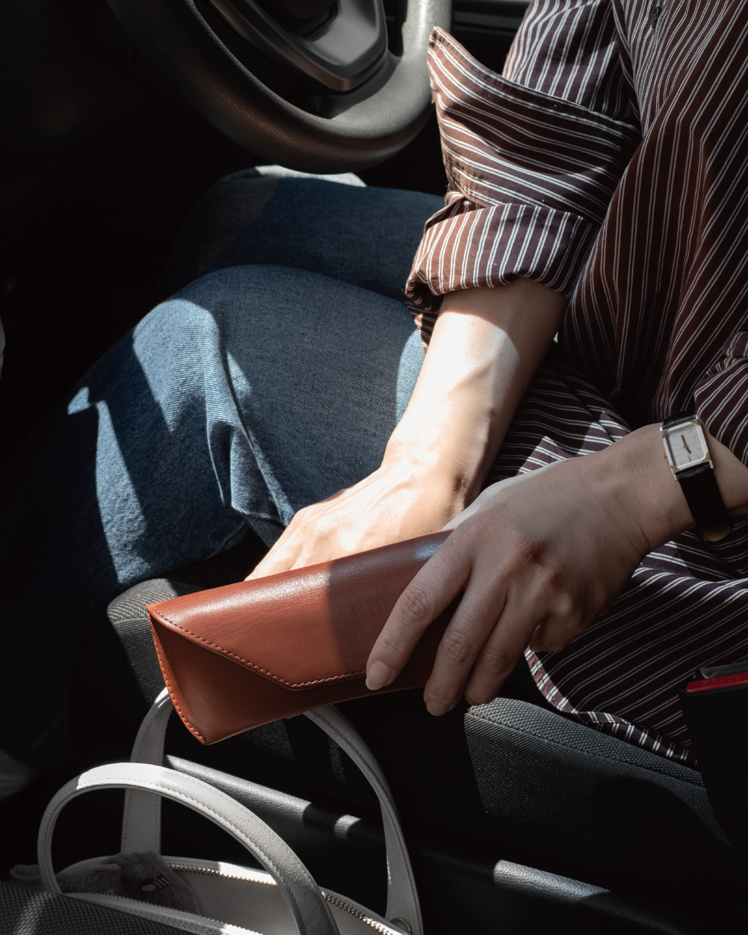 車内でモカブラウンの本革メガネケースを手に持つシーン、ドライブ中の眼鏡収納にも馴染む落ち着いたカラーリング
