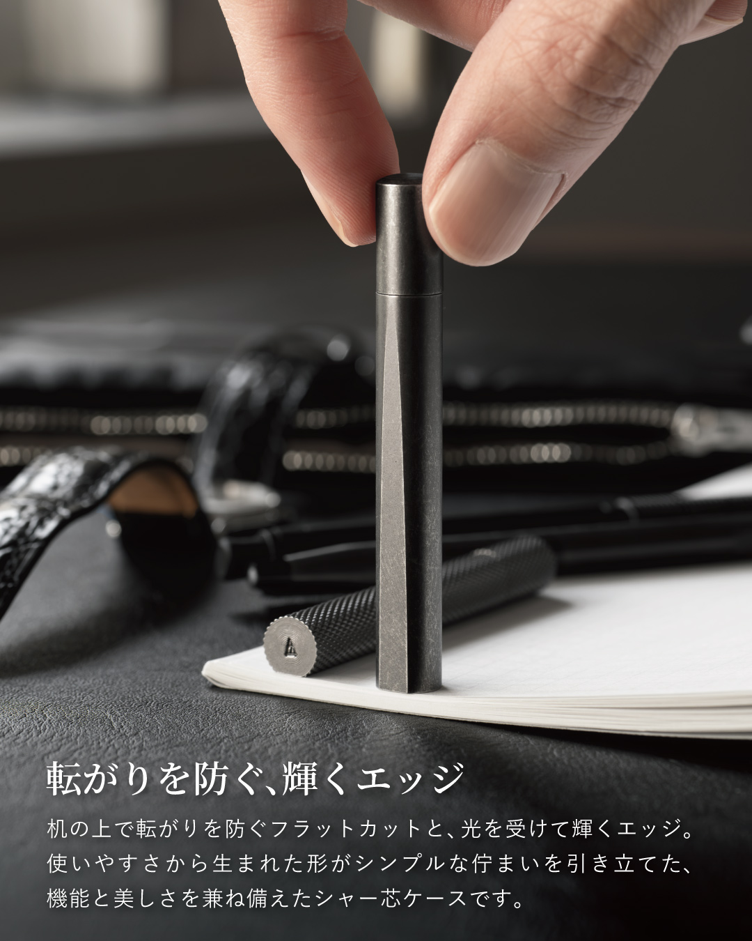 机に立てたブラックバレルのCRESIA シャー芯ケース、転がりを防ぐフラットカットと光を受けて輝くエッジ