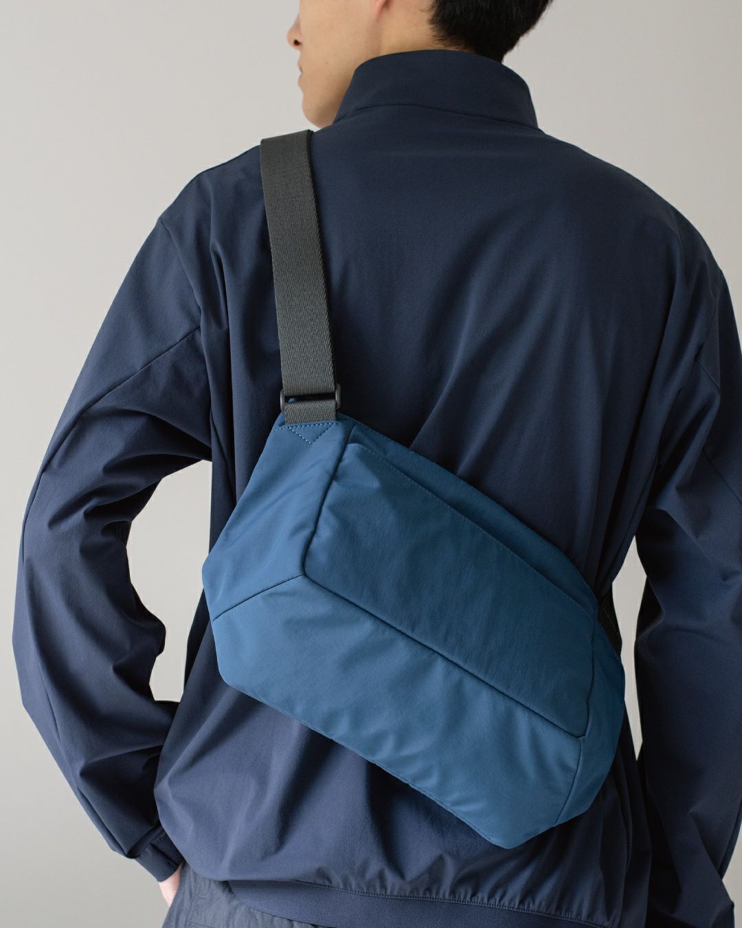 男性がネイビーのメンズショルダーバッグを背中に背負っている姿。バッグの背面からの見た目。