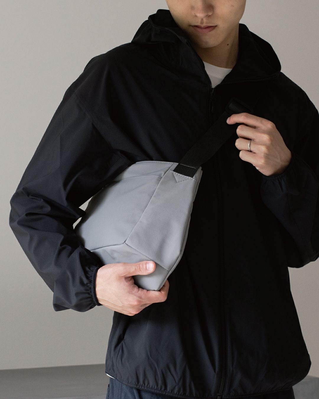 男性がライトグレーのメンズショルダーバッグを調整している様子。肩掛けのフィット感を表現。