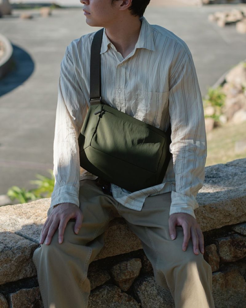 男性がカーキ色のメンズショルダーバッグを斜めがけにしているクローズアップ。