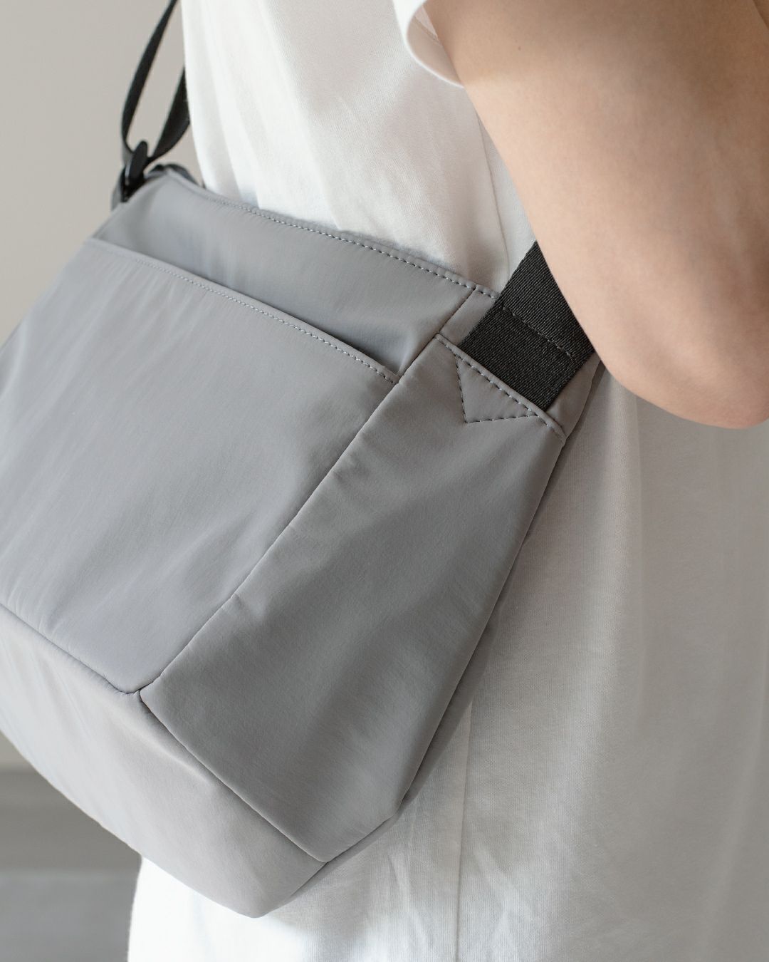 男性がライトグレーのメンズショルダーバッグを着用しているクローズアップ。バッグの素材感とシンプルなデザイン。