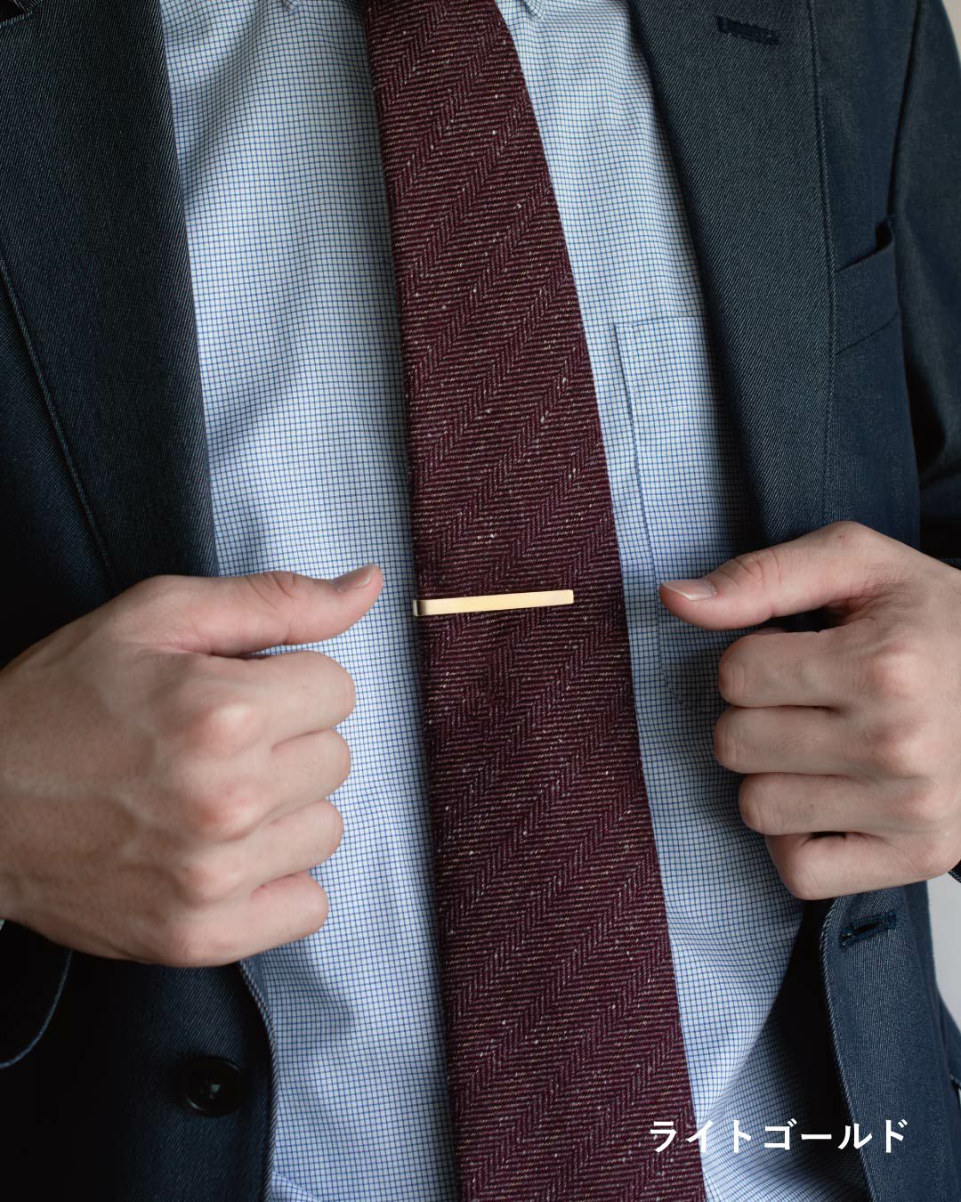 濃い赤色のネクタイにゴールドのネクタイピンを着用している男性の胸元と両手。