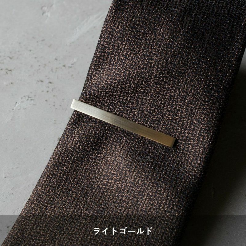 黒地に茶色の柄のネクタイに着用されたライトゴールドのシンプルなネクタイピン。