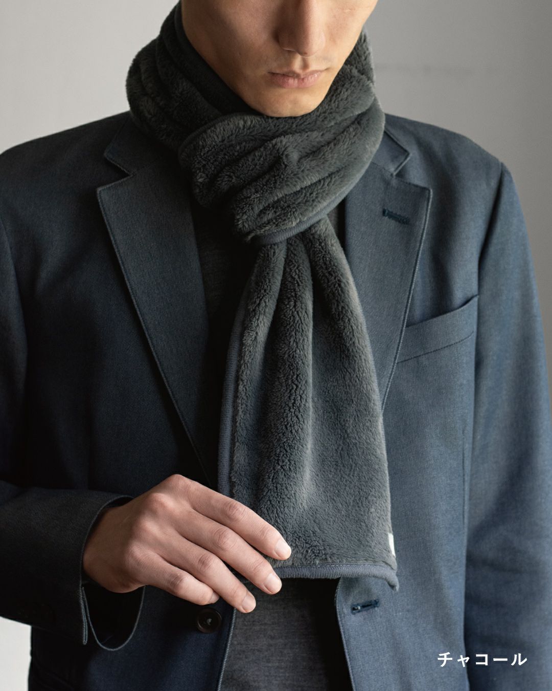 チャコール色の3秒マフラーを巻いた男性の着こなし。スーツやジャケットに合わせやすいフリース素材のマフラー。