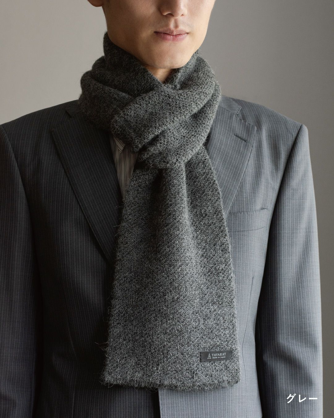 グレー色のアルパカ100%マフラーを巻いた男性の着こなし。シックな色味でスーツに合わせやすいビジネスマフラー。