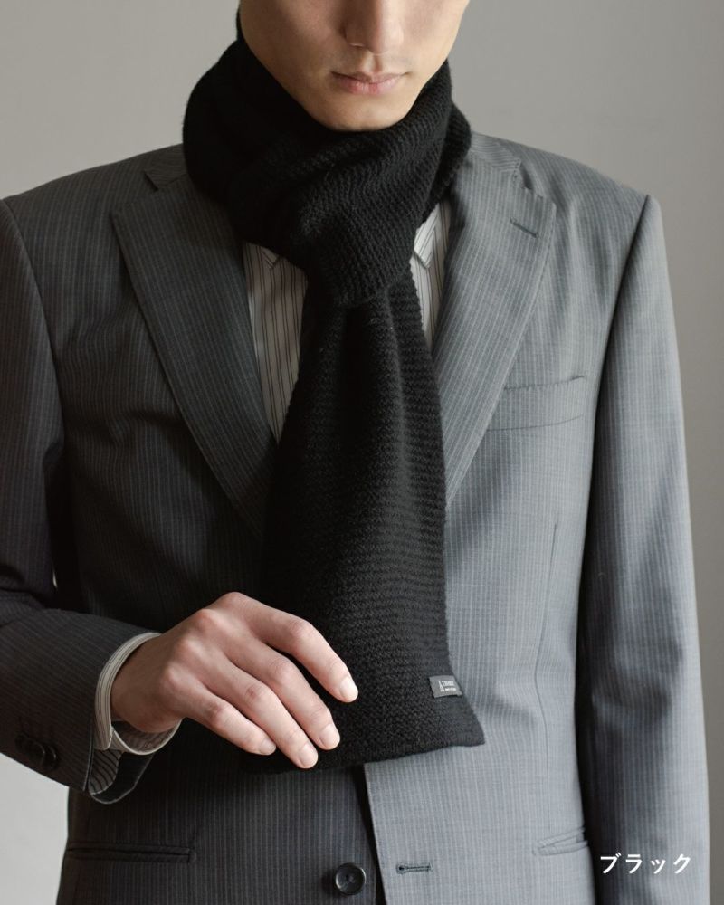 ブラック色のタック編みマフラーを巻いた男性の着こなし。フォーマルにも使えるラムウール混紡マフラー。