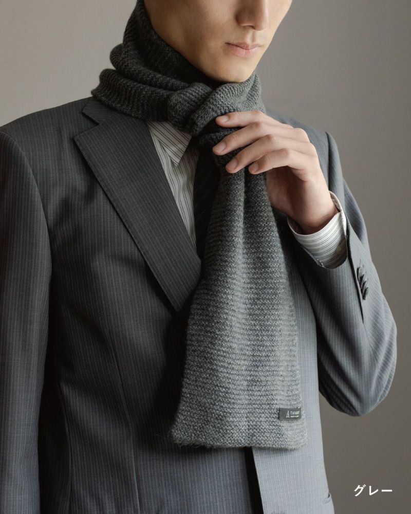 グレー色のタック編み 3秒マフラーを巻いた男性の着こなし。ビジネススーツに合わせやすい色と編み地。
