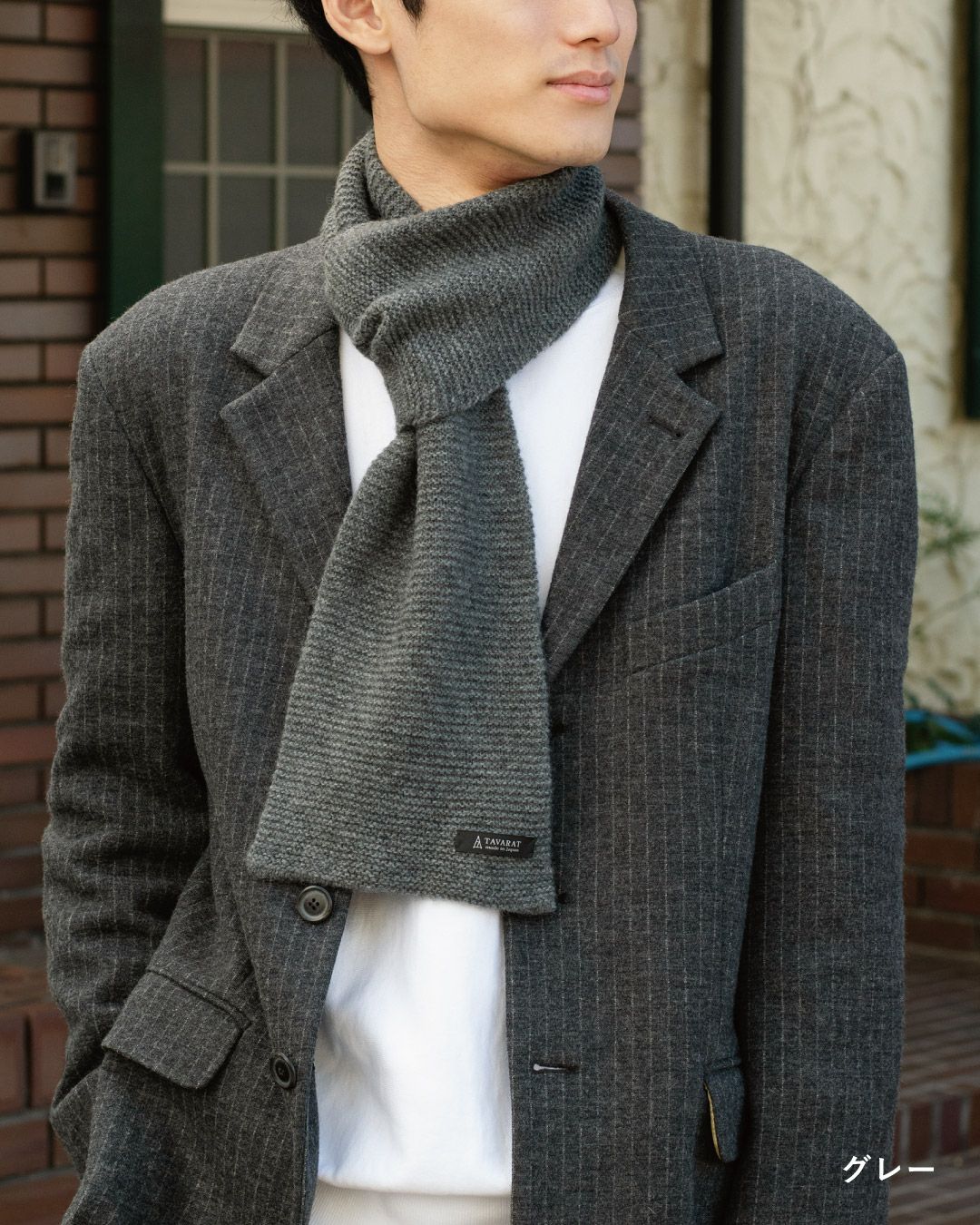 グレー色のタック編み 3秒マフラーを巻いた男性の着こなし。ビジネススーツに合わせやすい色と編み地。